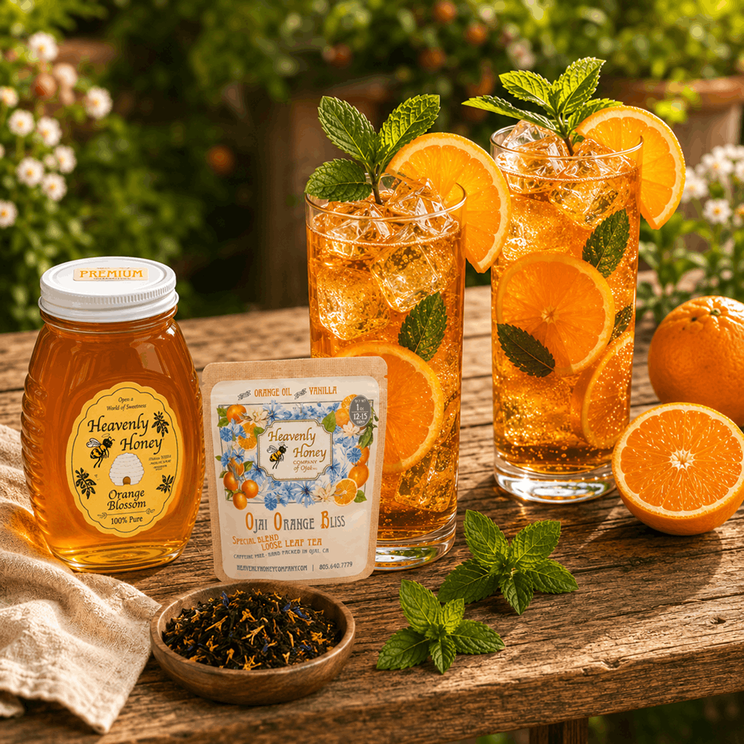 Two tall, condensation-covered glasses of golden-orange Ojai Pixie Orange Bliss Sparkler iced tea on a sunny outdoor wooden table, garnished with fresh tangerine wheels and mint, with a rustic bar of Ojai Orange Bliss Soap resting nearby.